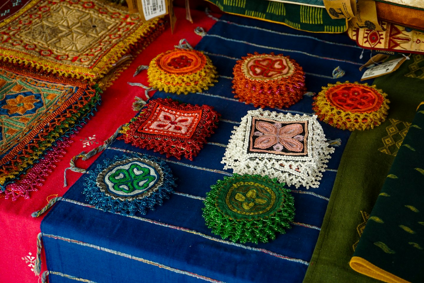 Handcrafted embroidered pouches and coasters arranged on fabric.