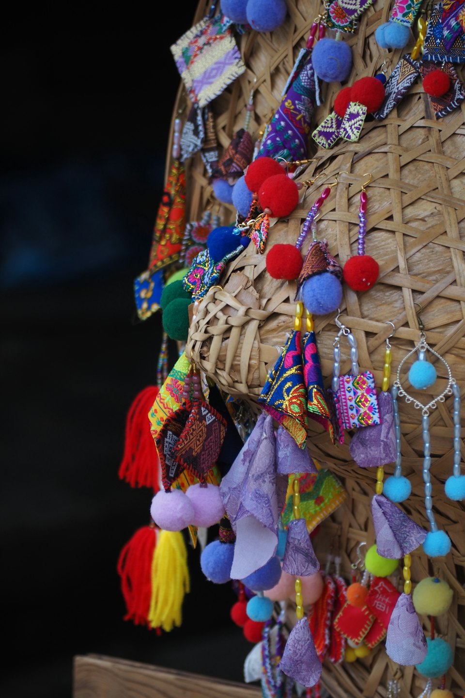 Colorful handmade earrings and trinkets displayed on woven fiber.