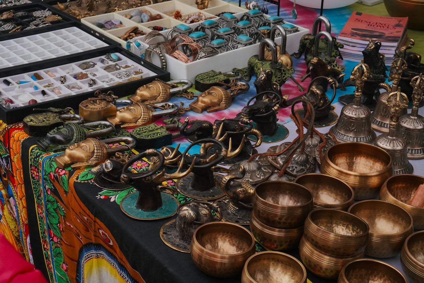 Market stall table with silver jewelry, brass locks, and singing bowls.