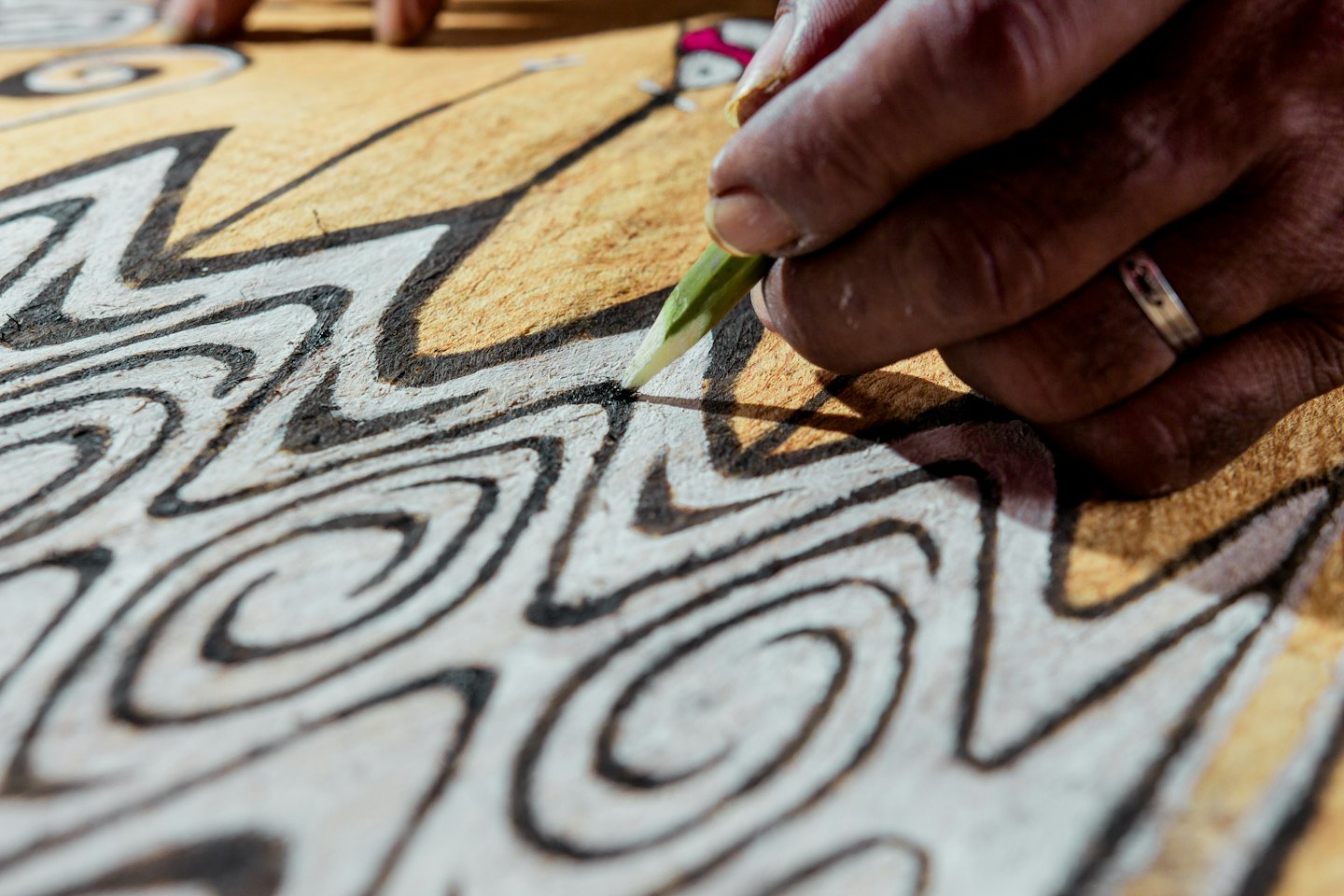 An artisan draws intricate patterns on a textured surface.