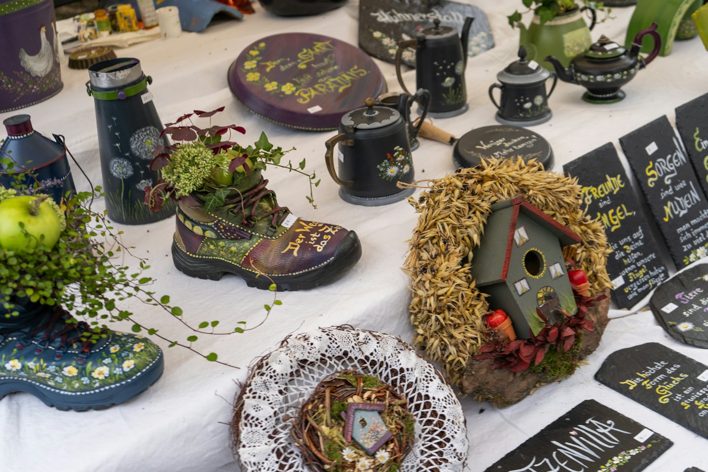 Handmade crafts including painted boot planters and slate plaques on display.